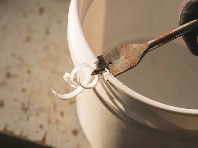A spade bit cutting a hole through the wall of a plastic pail